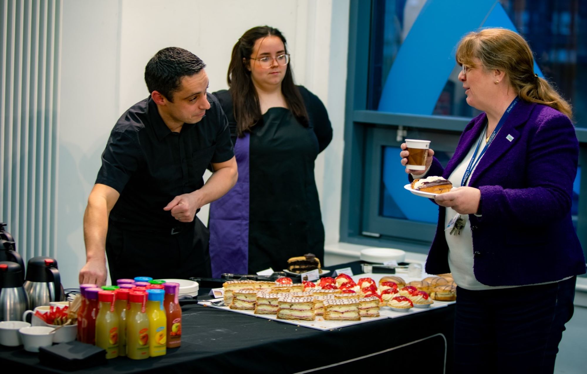 Catering team serving cream cakes and drinks behind a table