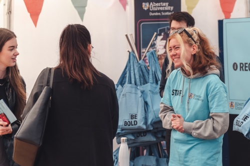 Two girls speaking to a smiling event helper at in information table