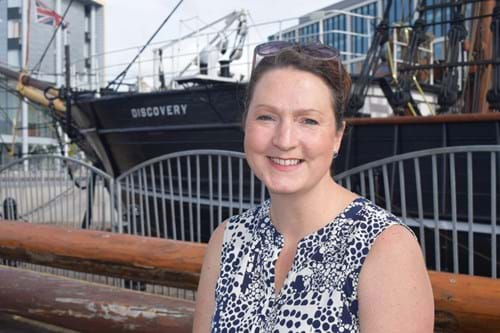 Rebecca Wade close up, next to the Discovery ship, smiling at the camera