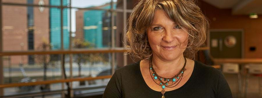 The image shows Dr Kate Smith of Abertay wearing a black dress and green necklace.