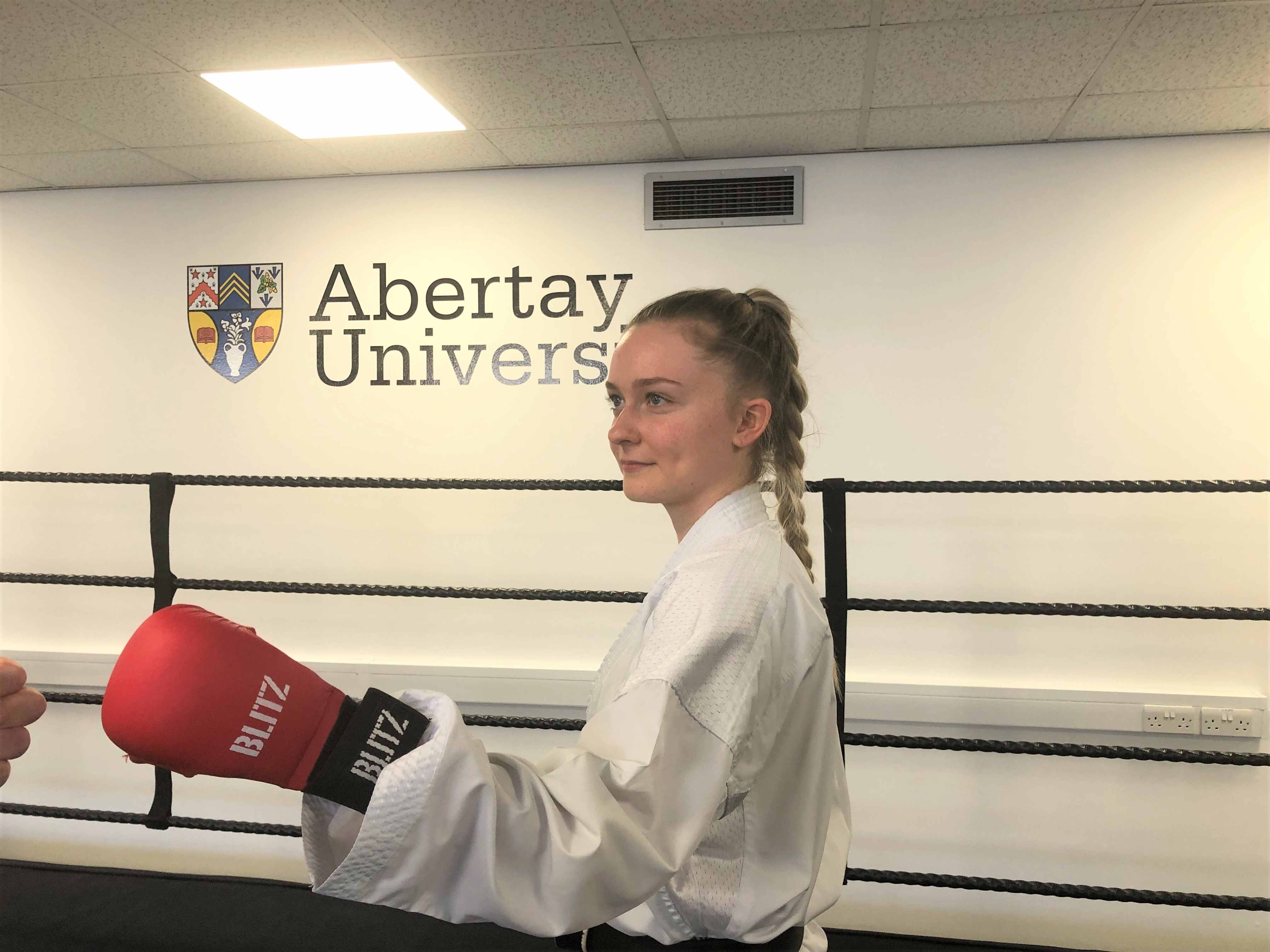 A female karate student with red boxing gloves on standing in a ring